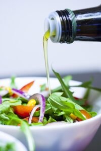Azeite de Oliva sendo derramado sobre uma salada fresca, representando seus benefícios para o emagrecimento.