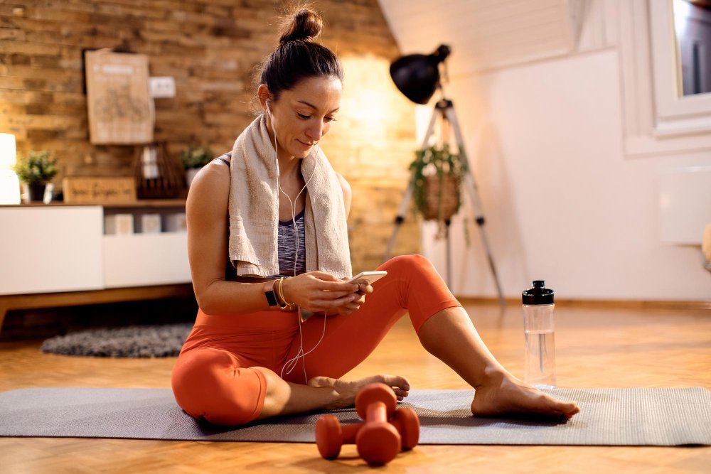 Atleta feminina usando telefone inteligente enquanto relaxa no chão em casa